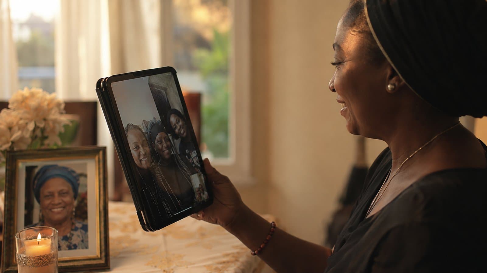 A woman smiling while on a video call with family, a lit candle and a photo of a loved one nearby
